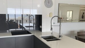 Une cuisine moderne dotée d’un grand îlot central, d’un lave-vaisselle encastré et offrant une vue sur la ville grâce à de grandes fenêtres.