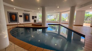 Une piscine intérieure avec des parois en verre transparent, un sol carrelé et une vue sur la verdure environnante.