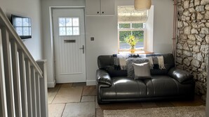 A living room with a stone wall, a black leather sofa, a hanging light fixture, and a door with a window. - Penderyn Cottage, Waterfall Country, Brecon Beacons (Aberdare)