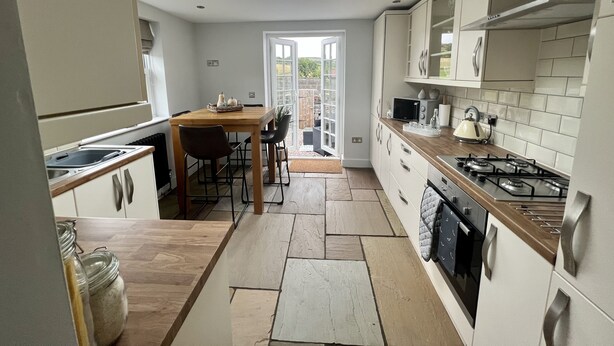A modern kitchen with a skylight, a dining area with a table and chairs, and a view through a glass door to an outdoor area. - Penderyn Cottage, Waterfall Country, Brecon Beacons (Aberdare)