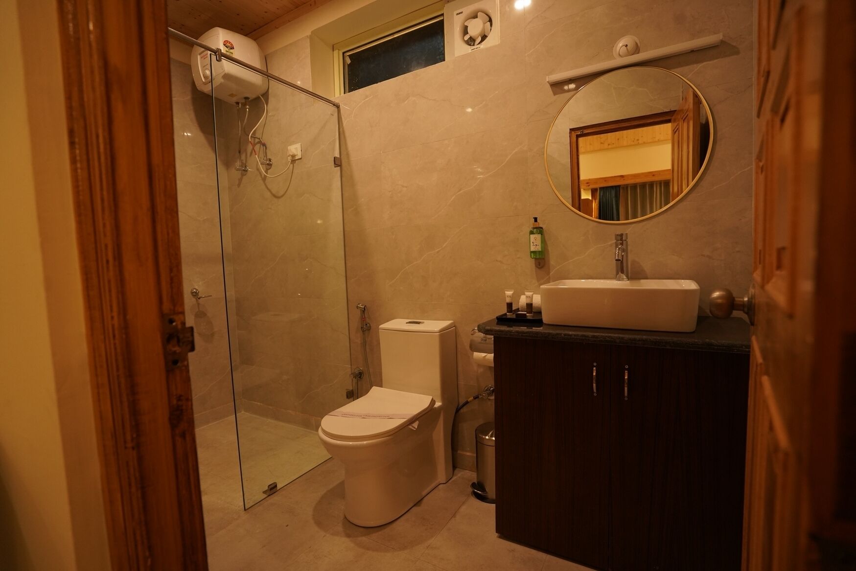 Un bagno con doccia vetrata, un WC, un lavandino con specchio e una piccola finestra sopra il lavandino.
