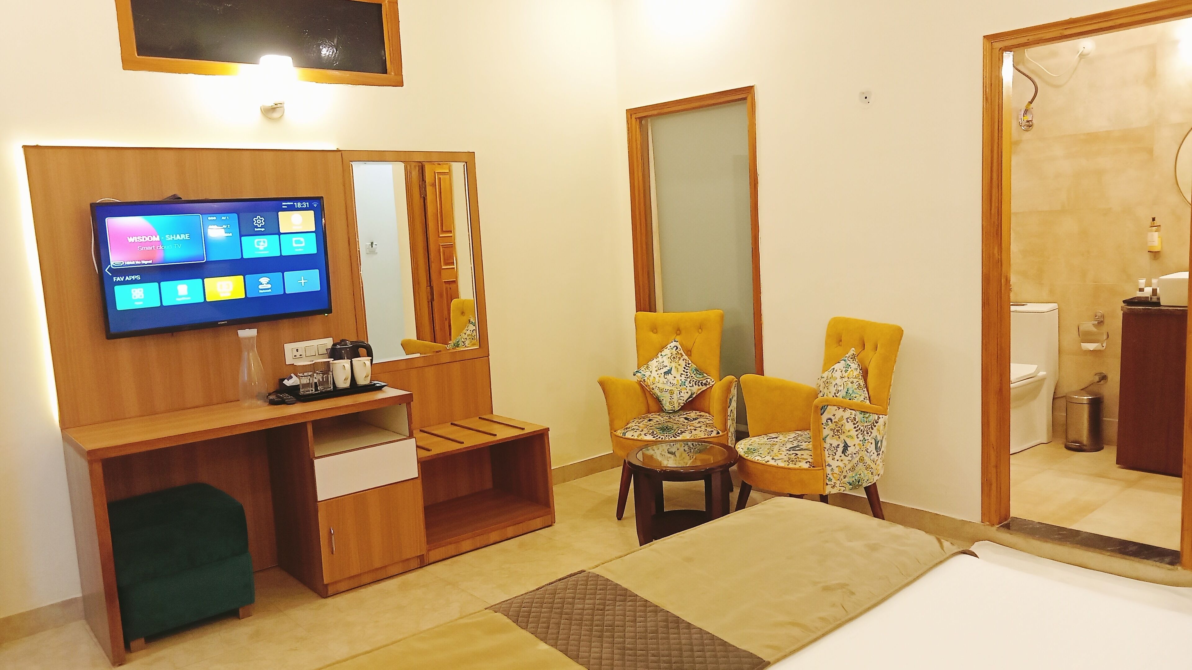 A modern living room with a flat-screen TV, wooden furniture, two yellow armchairs, a small table, and a mirror.