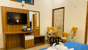 A hotel room with a bed, a TV, a desk with a chair, and a shower area. - HOTEL ALPINE MUSK (Tehri)