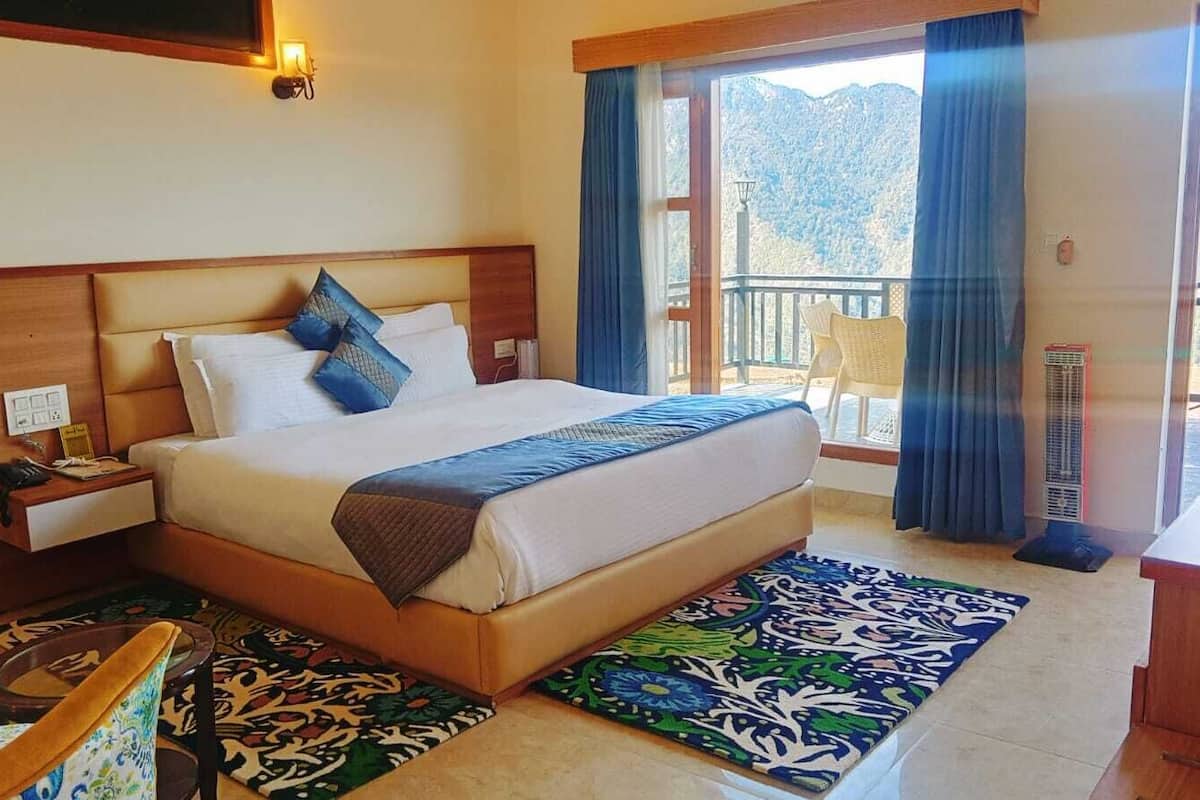 A hotel room with a bed, a nightstand, a chair, a desk, and a view of mountains through the window.