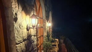 A stone building with arched windows and wall-mounted lights, a wooden chair, and a potted plant on a balcony. - HOTEL ALPINE MUSK (Tehri)