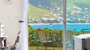 A room with a view of a coastal town, a chair, a guitar, and a bed.