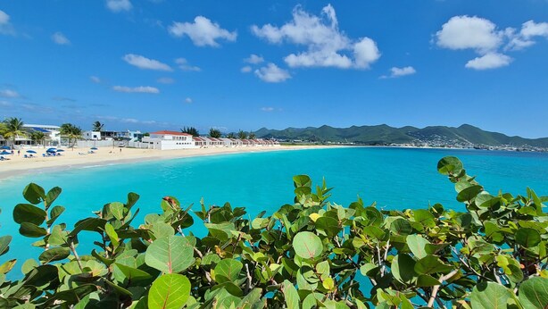 A beach with clear turquoise water, palm trees, and a view of mountains in the distance.