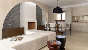 Ein modernes Wohnzimmer mit einer Couch, einem runden Couchtisch und einem Essbereich mit Stühlen und Tisch. Im Hintergrund befindet sich ein Kamin und eine Küche.