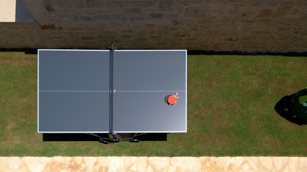 A ping pong table with a net in the middle, placed on a grassy lawn with a stone wall in the background.
