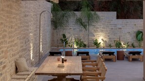 Ein Essbereich im Freien mit Steinwänden, einem Holztisch und -stühlen, einer eingebauten Bank und einem kleinen Pool.