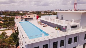 Relax by the rectangular pool surrounded by lounge chairs and a seating area with cushions, offering a view of the city.