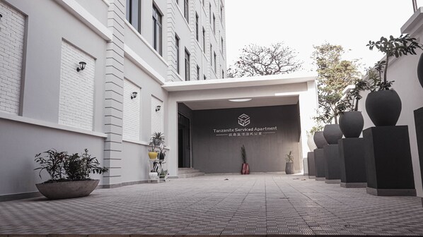 Welcome to Tanzanite Serviced Apartment, featuring a clean and minimalist entrance with a geometric pattern and lush greenery.
