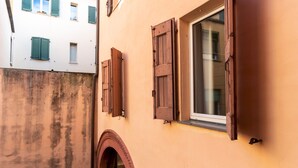 A narrow alleyway with a building featuring a large window with wooden shutters and a small arched doorway. - Italianway - San Vitale 87 (Bologna)