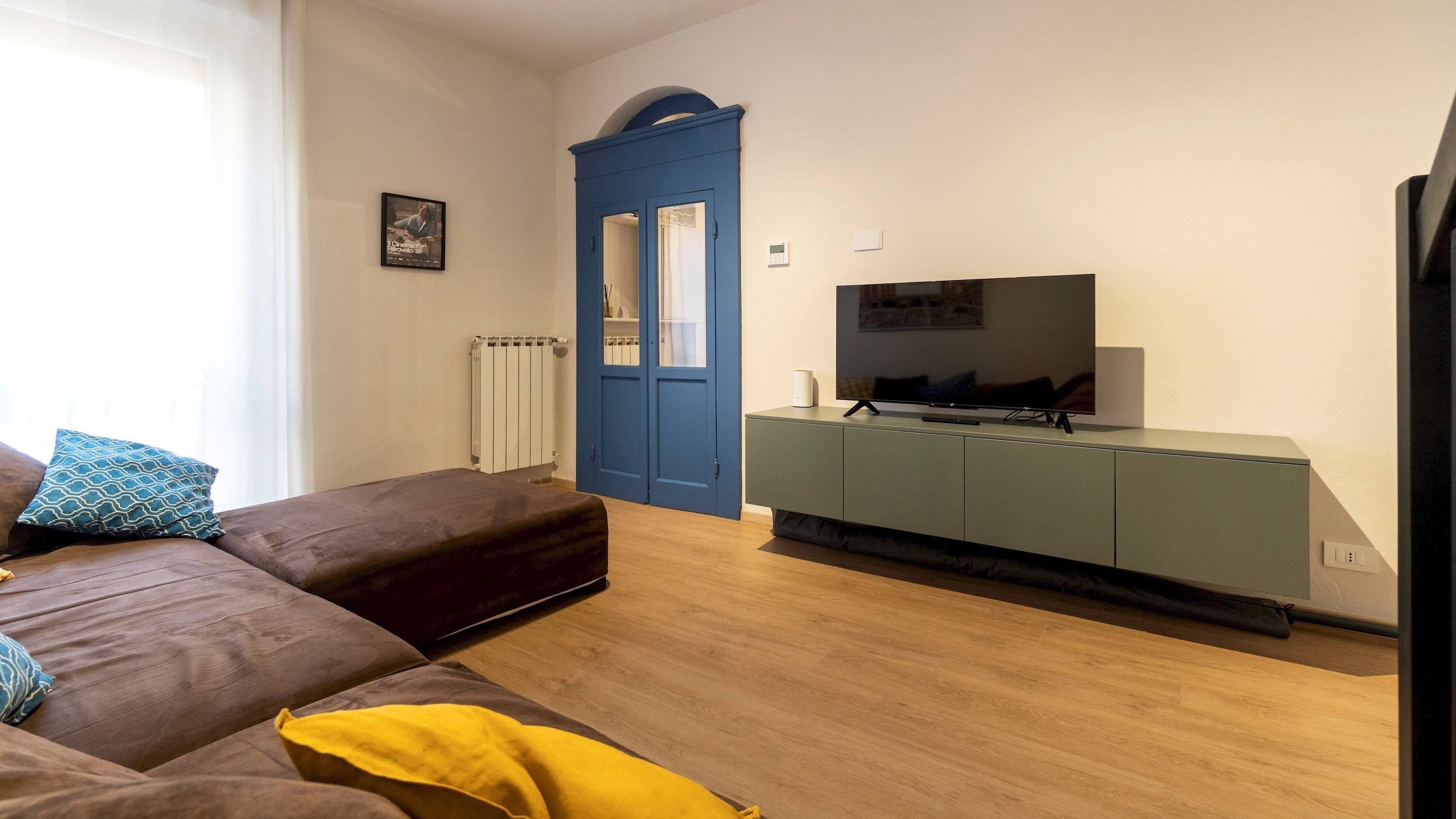 Una sala de estar moderna con un sofá marrón, una manta amarilla, una puerta azul y un televisor sobre un mueble.