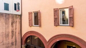 A building with two windows with wooden shutters, a stone wall, and an arched entrance. - Italianway - San Vitale 87 (Bologna)