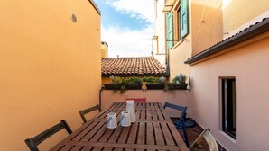 A narrow courtyard with a wooden table and chairs, a small window, and a tiled roof visible in the background. - Italianway - San Vitale 87 (Bologna)