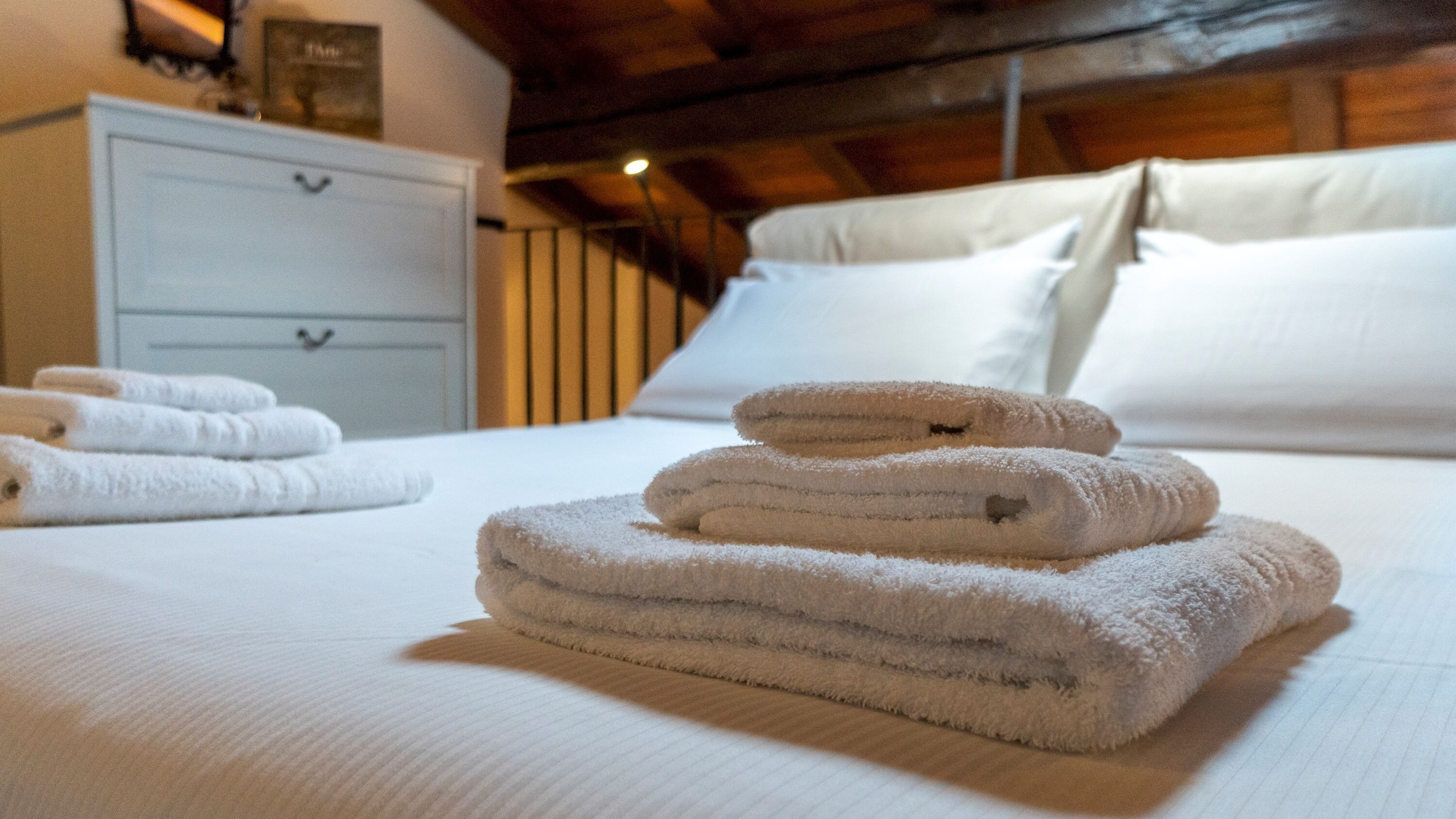 Ein ordentlich bezogenes Bett mit gefalteten Handtüchern und eine weiße Kommode im Hintergrund.