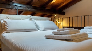 A neatly made bed with white linens and folded towels, wooden beams above, and a simple metal headboard. - Italianway - Piella 5 (Bologna)