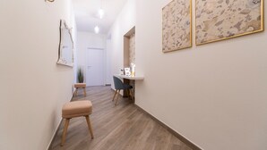 A hallway with a wooden floor, a bench, a desk with a chair, and two framed floral artworks on the wall.