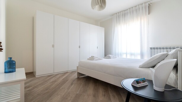 A modern bedroom with a bed, a wardrobe, a small table, and a blue vase.