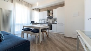 A modern kitchen with white cabinets, a dining table with two chairs, and a blue sofa in the living area.