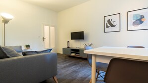 A modern living room with a grey sofa, a white table, and a TV on a stand. - Italianway - Baracca 7 A (Bologna)