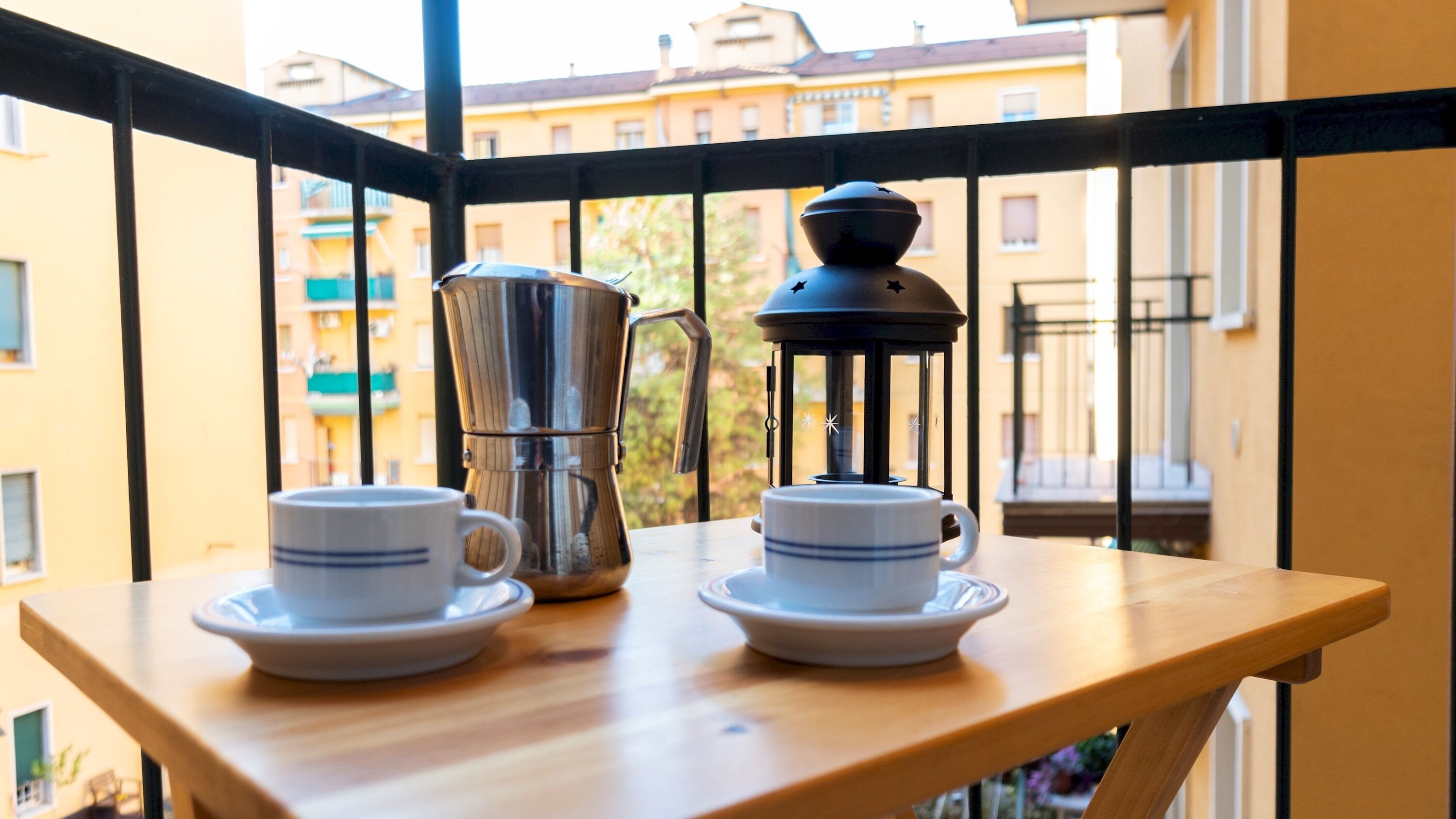 A balcony with a table holding two cups and a coffee maker.
