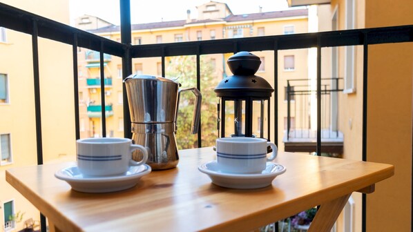 A balcony with a table holding two cups and a coffee maker.