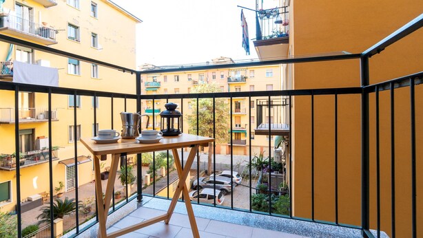 A balcony with a table set for tea, overlooking a courtyard with parked cars and buildings. - Italianway - Baracca 7 A (Bologna)