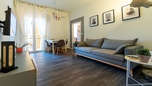 A modern living room with a grey sofa, a dining table with chairs, a TV, and artwork on the wall. - Italianway - Baracca 7 A (Bologna)