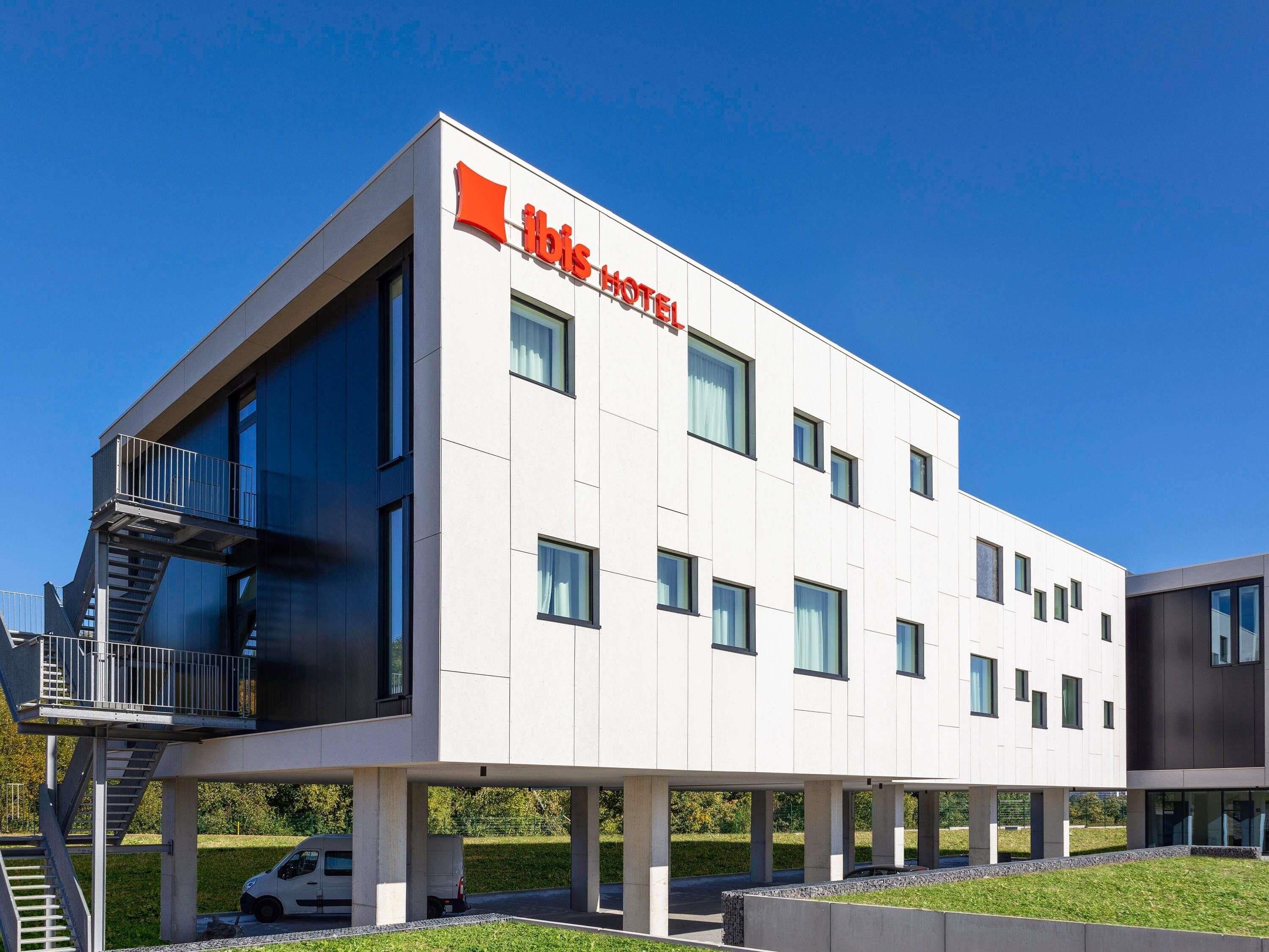 A modern hotel building with a flat roof, large windows, and a prominent logo.