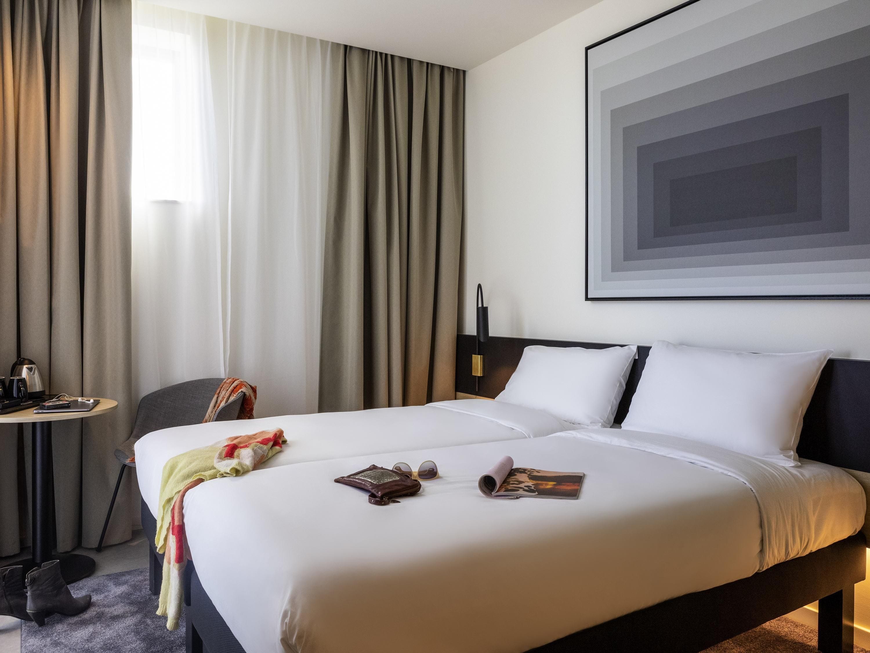 Quarto de hotel com uma cama grande, mesa de cabeceira, uma cadeira e uma obra de arte emoldurada na parede.