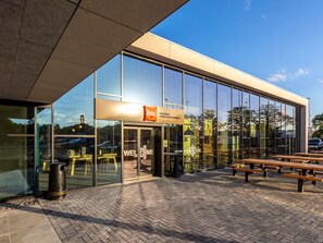 A modern building with large glass windows, a sign reading 'ibis Brussels Groot-Bijgaarden,' and outdoor seating. - Ibis Brussels Groot Bijgaarden (Dilbeek)