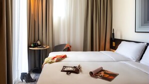 Una habitación de hotel con dos camas, una mesita con una lámpara y una silla.