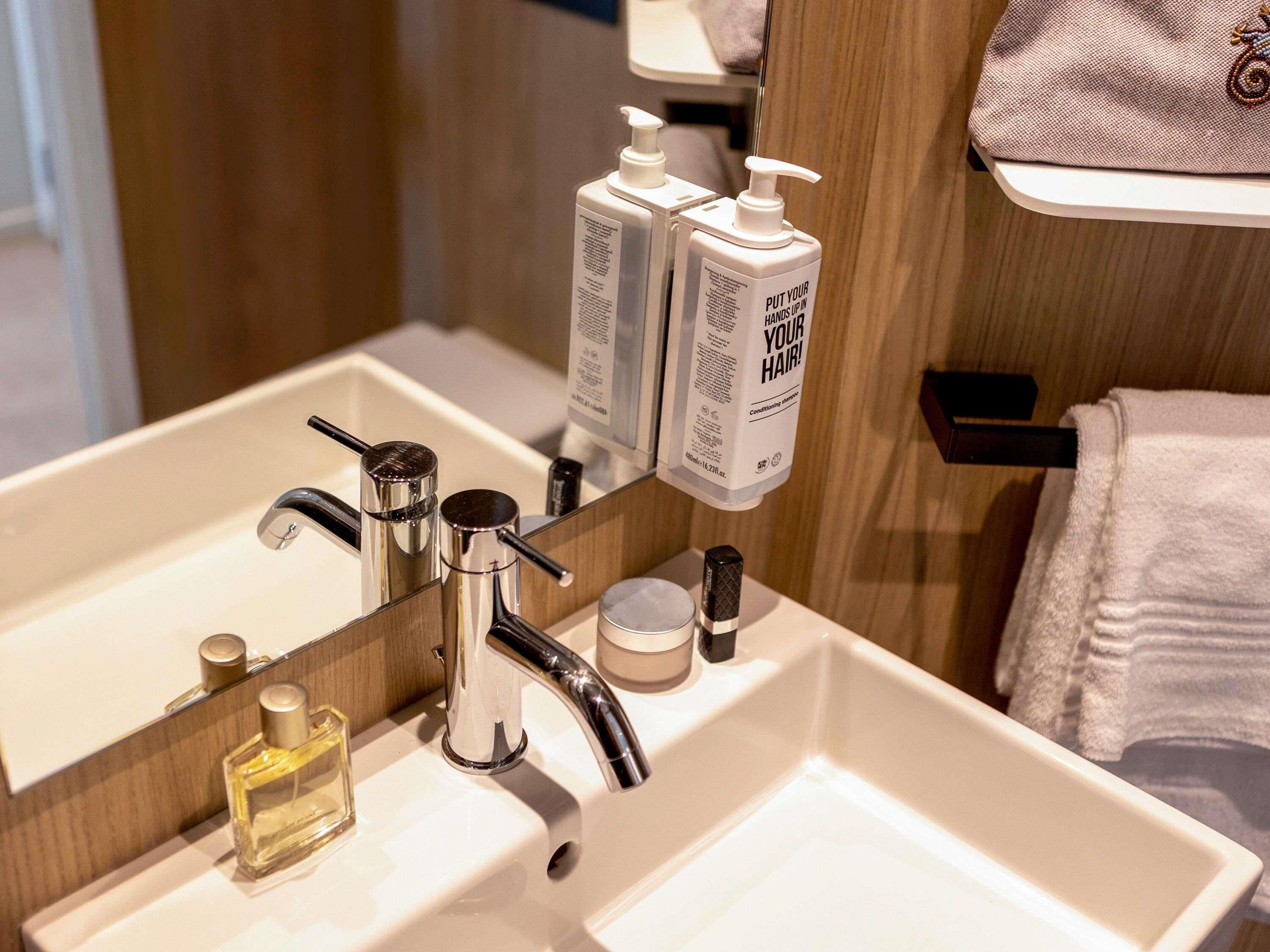 Un lavamanos de baño con espejo, grifo y dos dispensadores de jabón.
