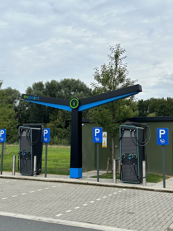 A parking area with EV charging stations, marked by blue signs with a 'P' and a plug symbol.