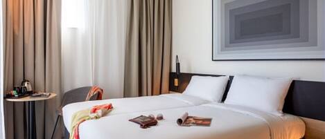 Quarto de hotel com cama grande, uma pequena mesa com chaleira e uma cadeira.