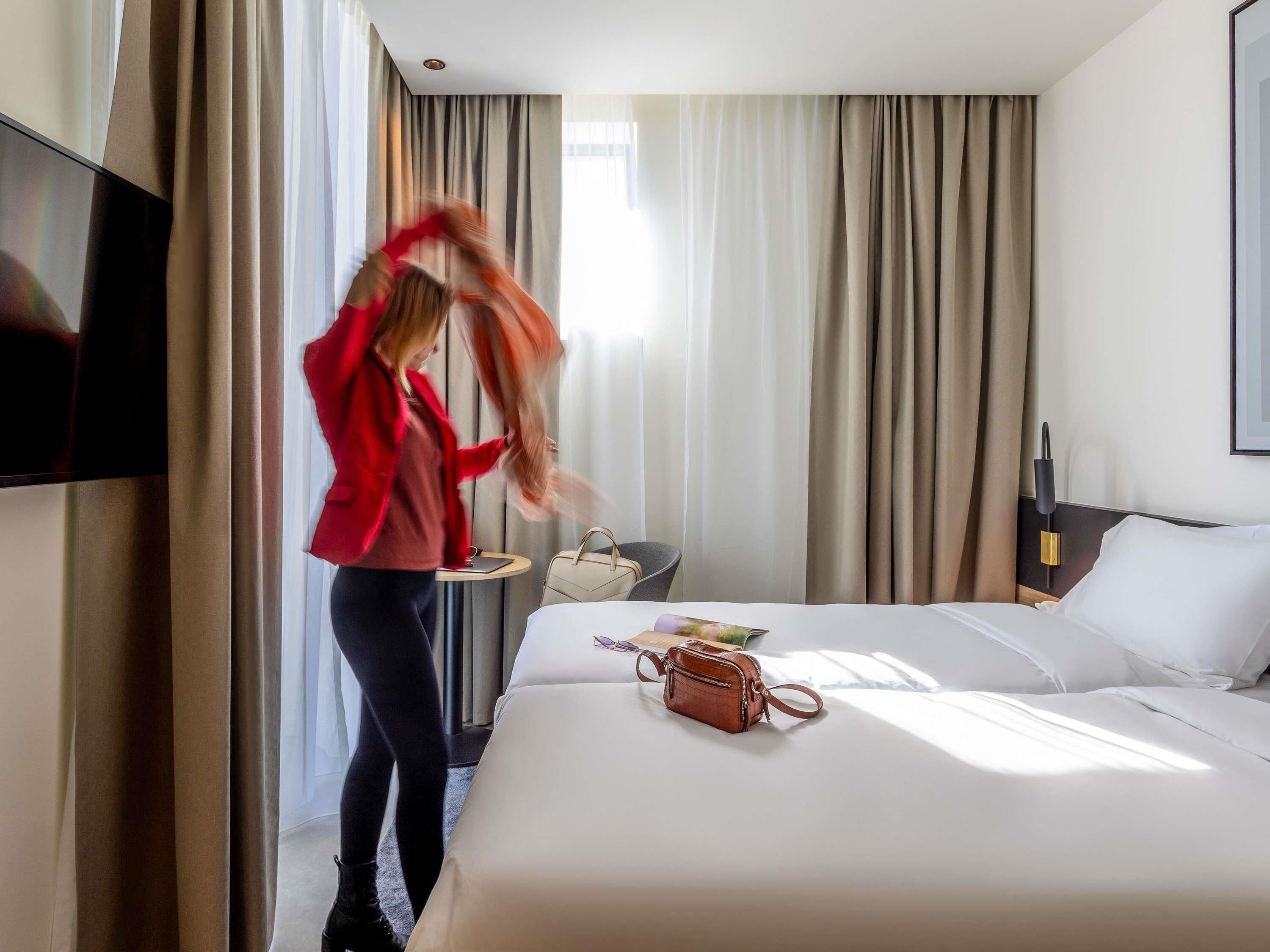 Een hotelkamer met een bed, een stoel, een klein tafeltje en een aan de muur bevestigde televisie.