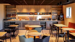 Una cafetería moderna con mobiliario de madera, una barra central con una exposición de frutas, y un área de estar con mesas y sillas redondas.