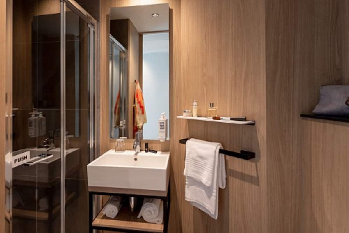 A modern bathroom with a glass shower enclosure, a white sink, and a wooden vanity with towels.