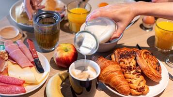 Une table de petit-déjeuner avec divers aliments, notamment des viennoiseries, du fromage et un verre de jus d’orange.