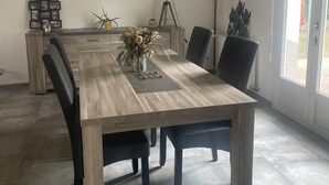 Un coin repas avec une longue table en bois, des chaises noires, un vase de fleurs, une décoration en forme de poisson et un tableau encadré au mur.