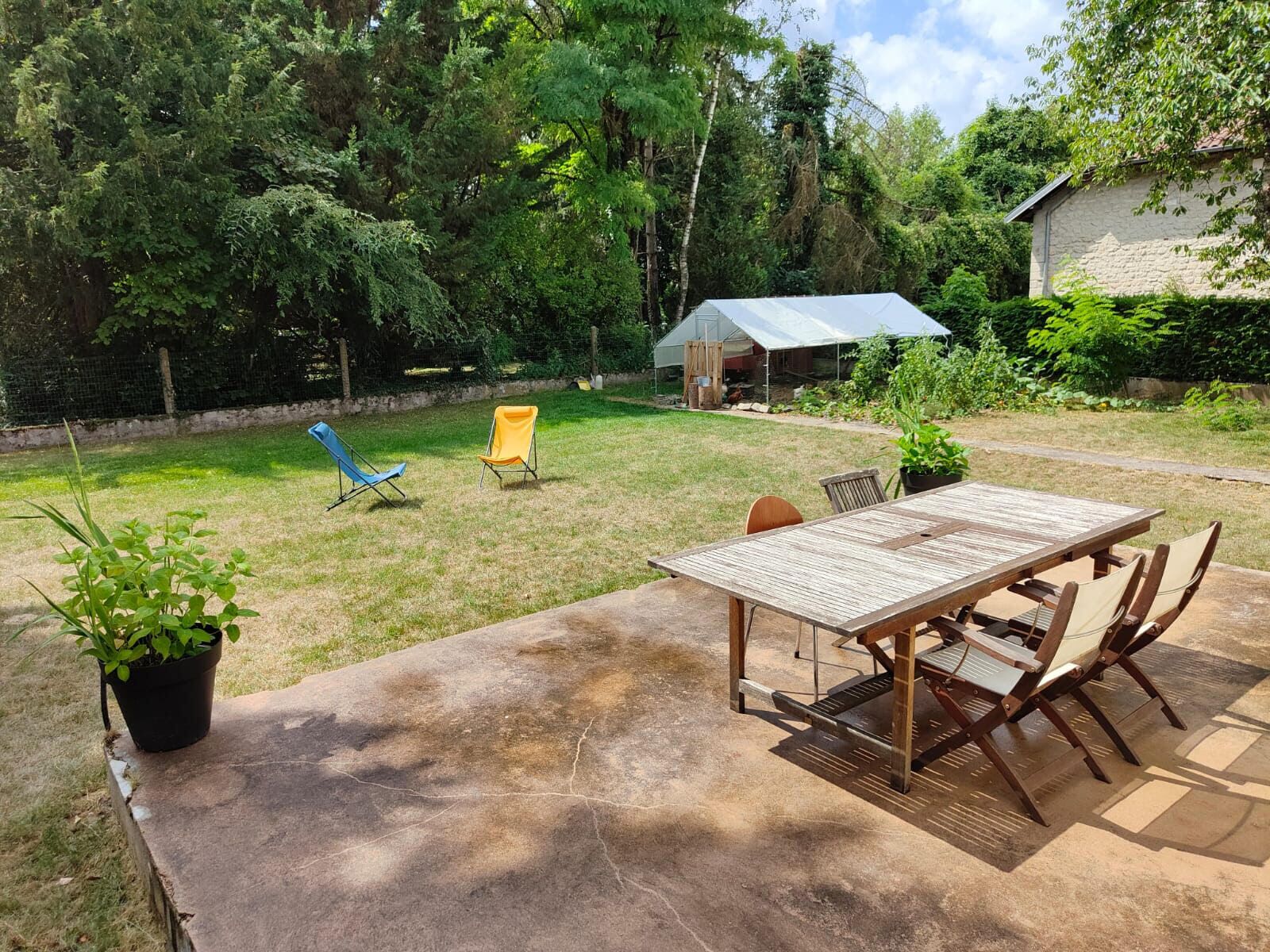 Une terrasse avec une table et des chaises, entourée d’une pelouse et d’arbres.