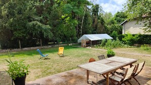 Une terrasse avec une table et des chaises, entourée d’une pelouse et d’arbres.