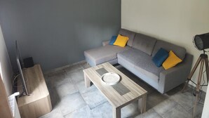 Un salon moderne avec un canapé d’angle gris, une table basse en bois et une petite table d’appoint.