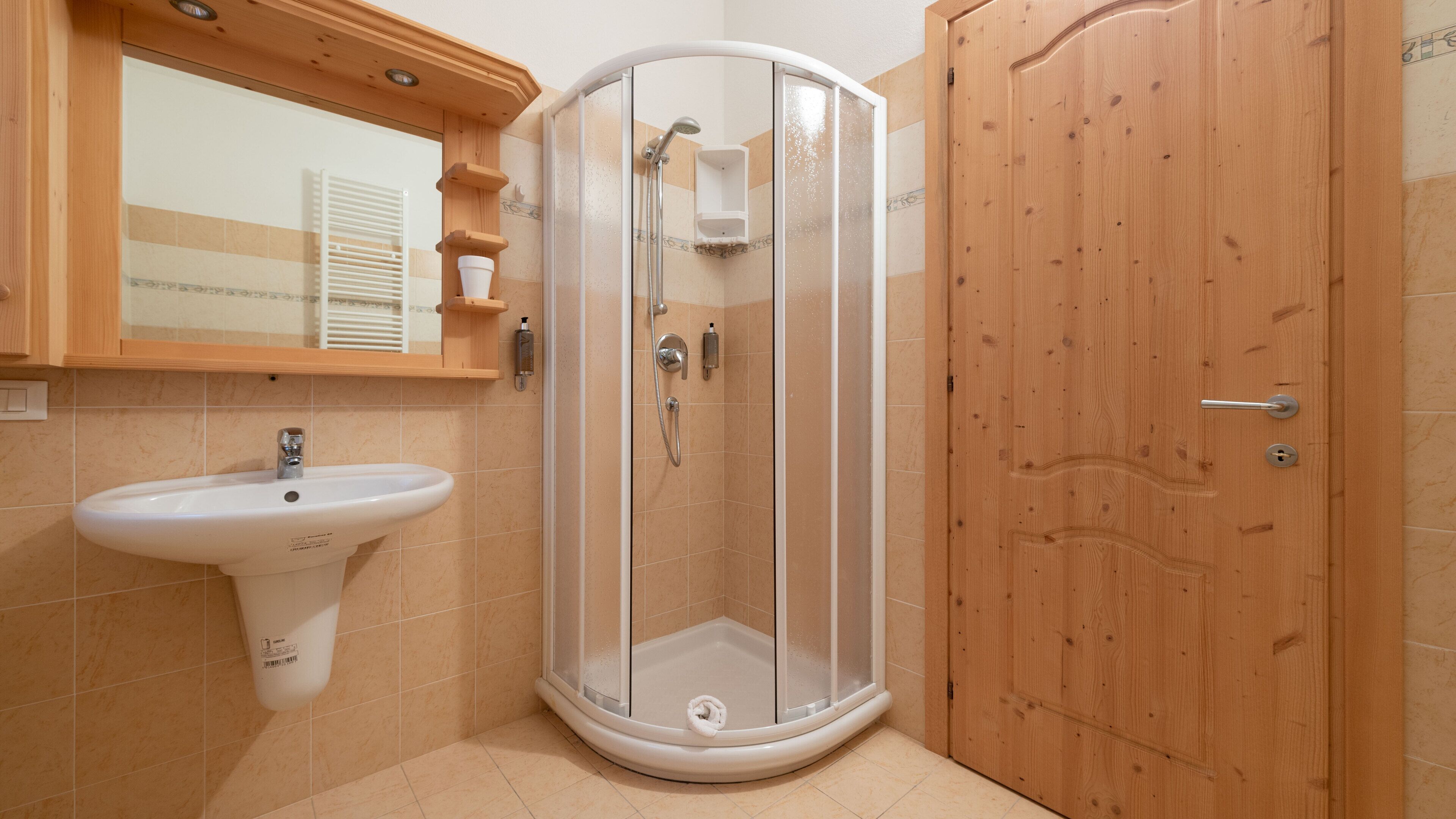Een badkamer met een douchecabine van glas, een witte wastafel en een houten deur.