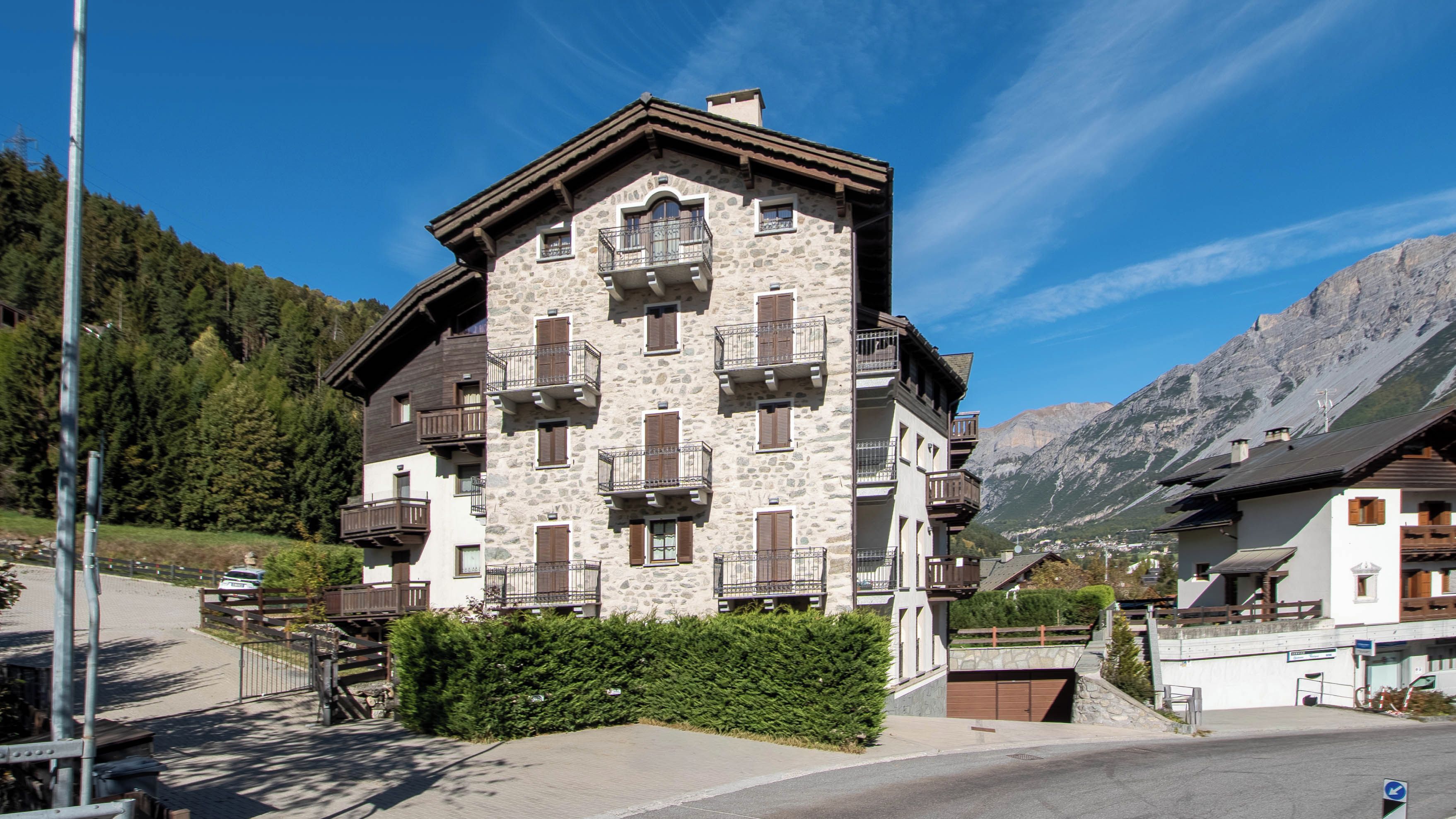 A multi-story building with balconies, set against a mountainous backdrop.