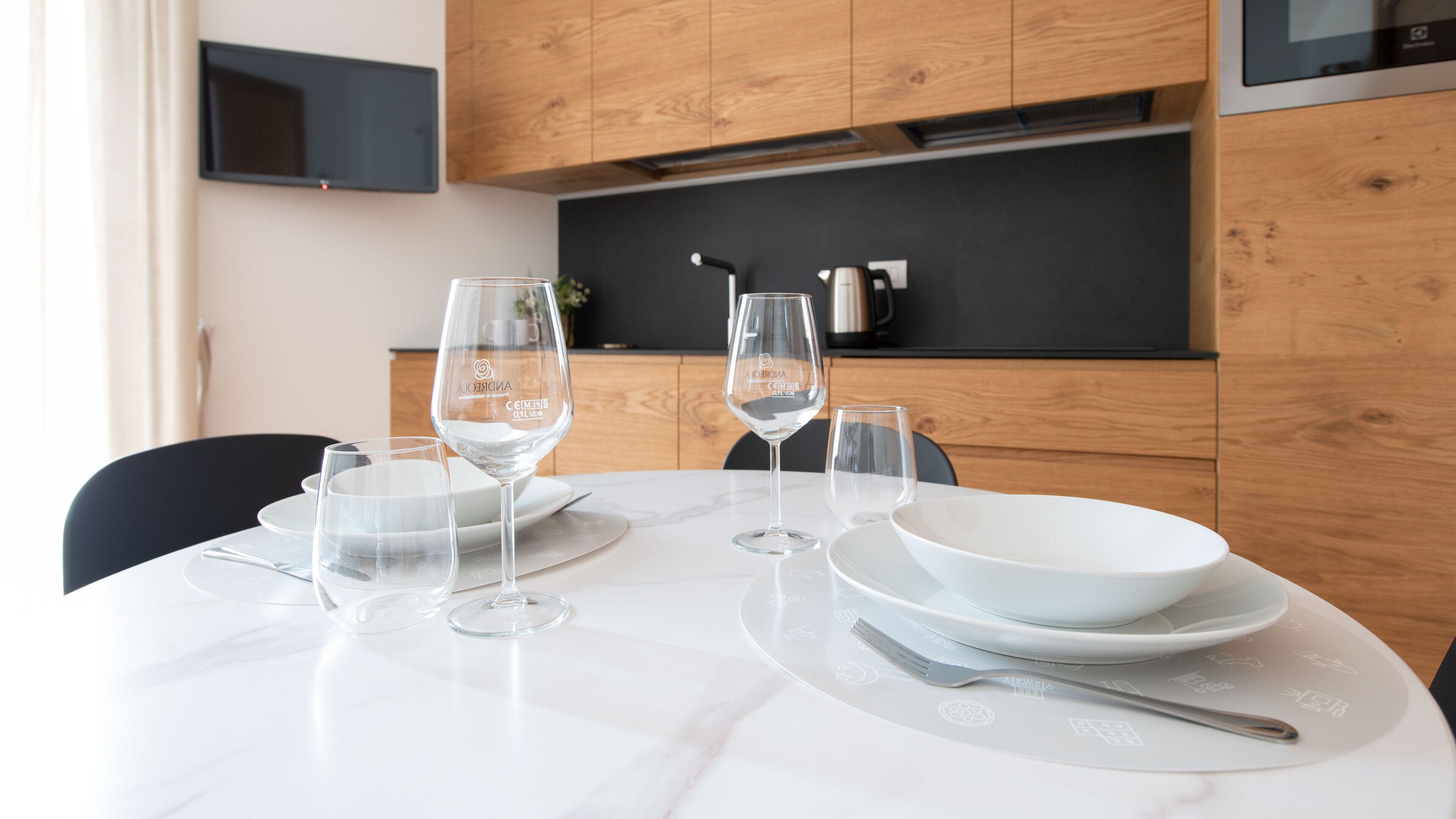A dining table set with white plates, clear wine glasses, and a bowl.