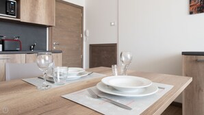 A dining table set with plates, glasses, and cutlery, with a wooden table and a kitchen in the background. - Ciuk 11 (Valdisotto)