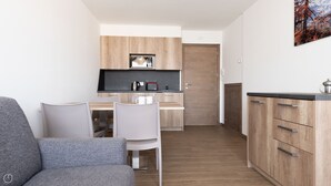 A compact living space with a kitchenette, a dining area with a table and chairs, and a grey sofa. - Ciuk 11 (Valdisotto)